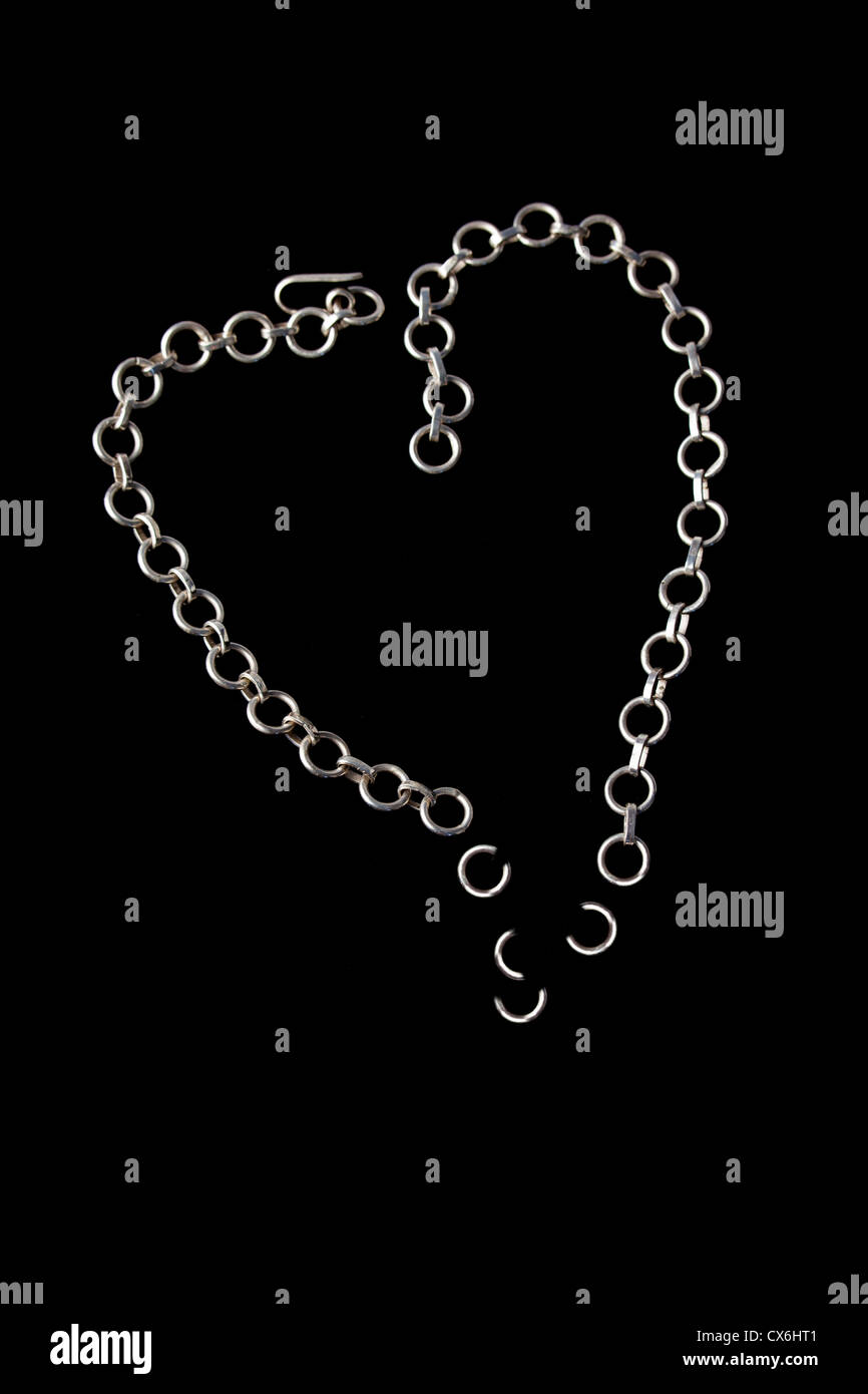 Broken shattered silver chain neckless in heart shape on pure black background Stock Photo