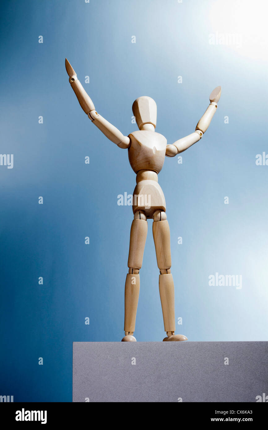 An artist's figure standing atop a box with arms raised and head tilted up Stock Photo