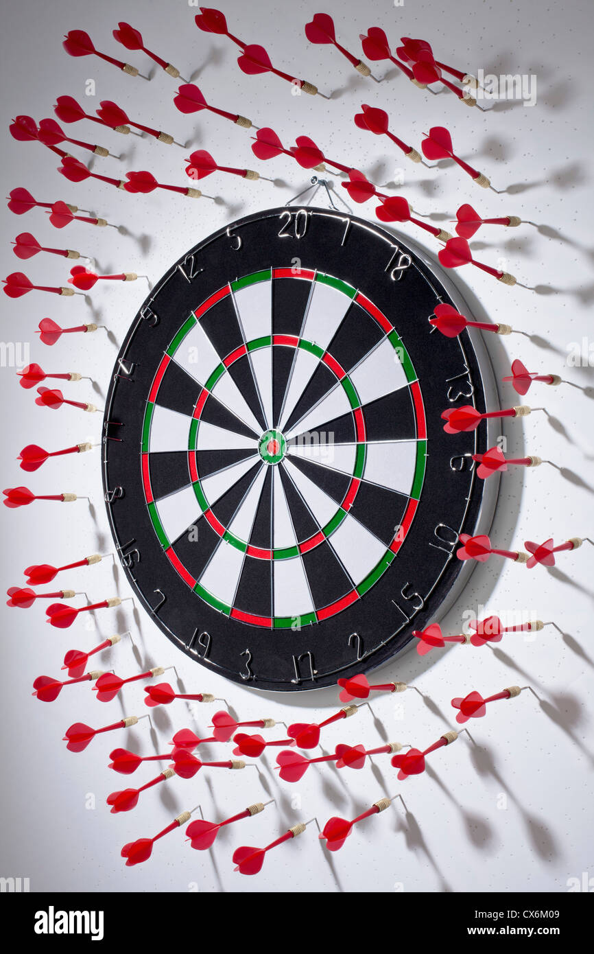 Multiple darts stuck in a wall all around a dartboard Stock Photo Alamy