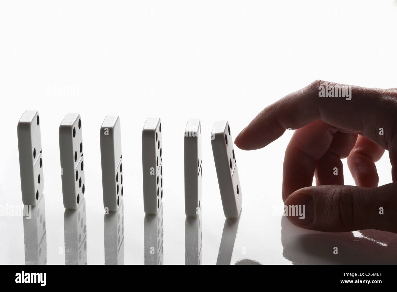 A man pushing the first domino in a row, focus on hand Stock Photo