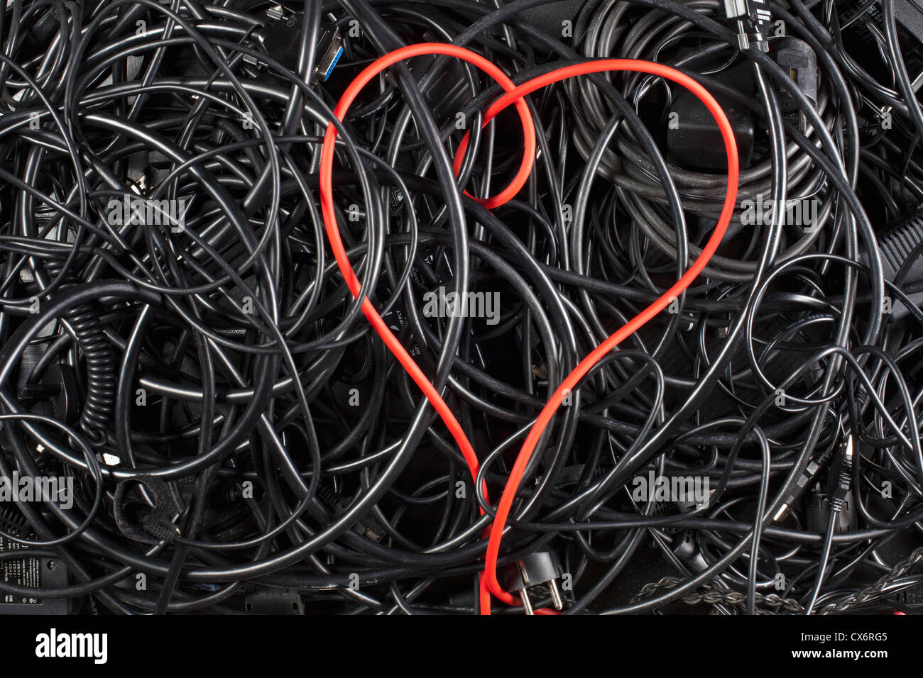 A red cord in a heart shape amongst tangled black cables and cords Stock Photo