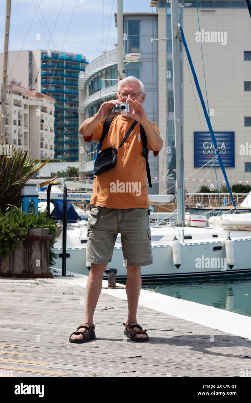 Senior man tourist taking photos using compact camera. Ocean Village, Gibraltar, UK. Stock Photo
