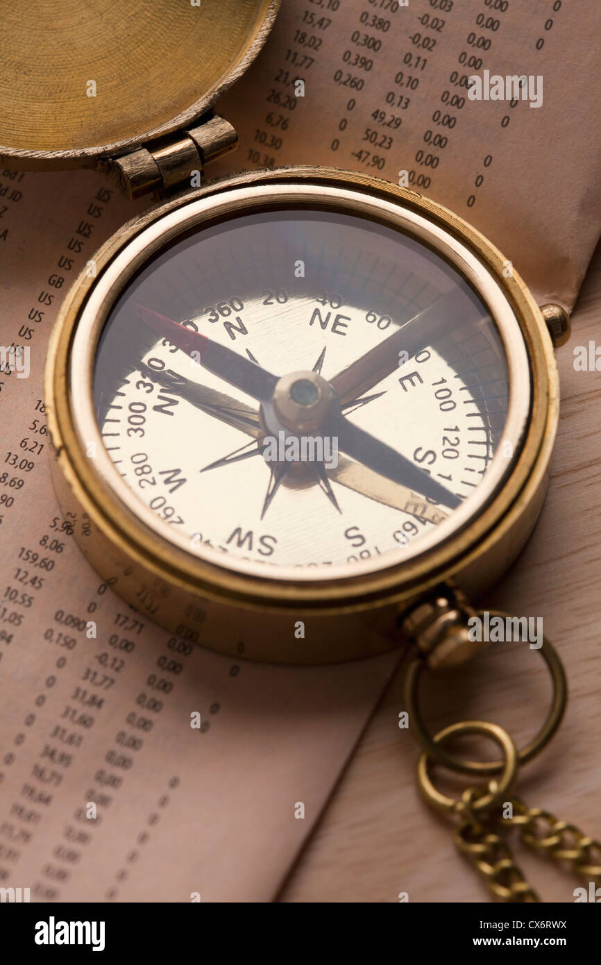 A brass pocket compass on top of the financial page of a newspaper Stock Photo