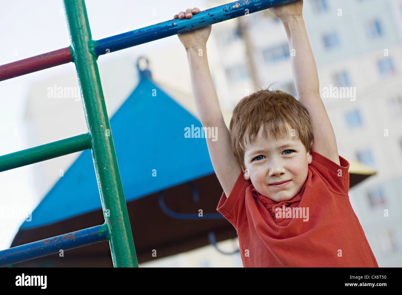 A boy hanging from a playground bar Stock Photo
