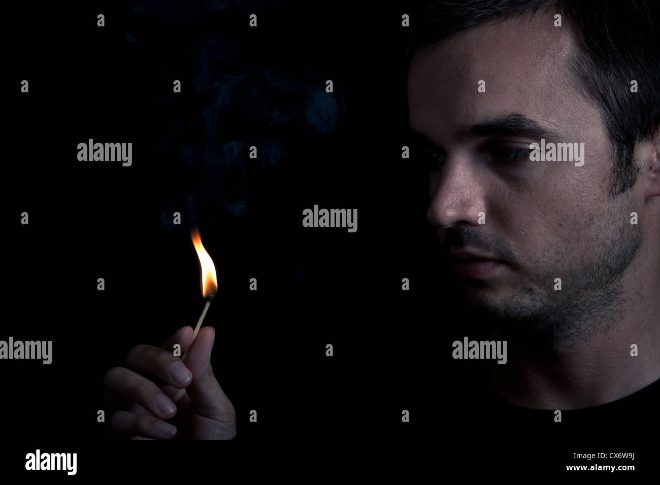 Dramatic portrait of man lighting safety match, over black background. Stock Photo