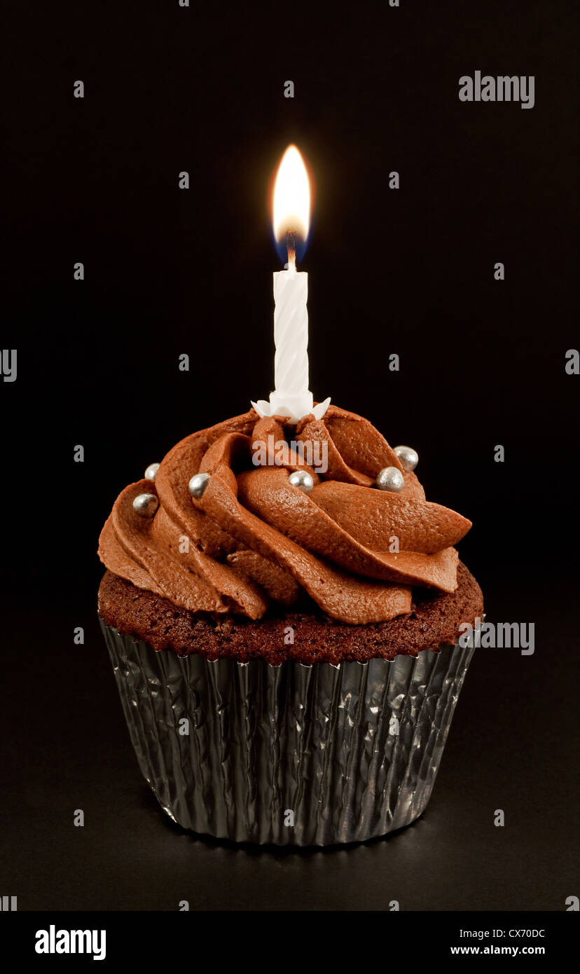 A home baked chocolate cup cake with a single lit candle to celebrate a birthday or other anniversary Stock Photo