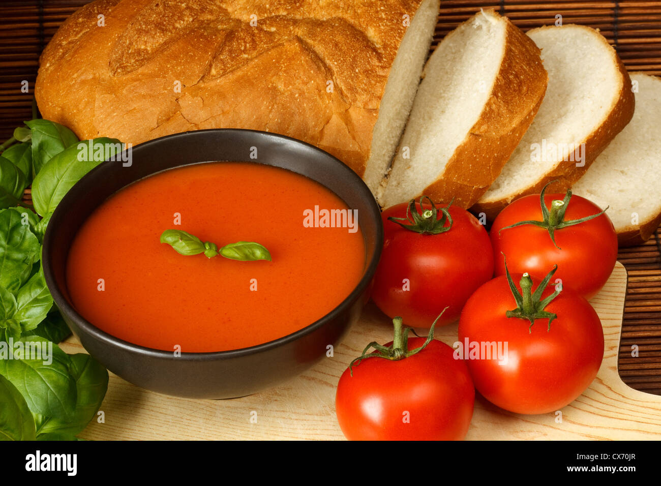 Bowl of tomato soup with basil garnish, in kitchen setting surrounded