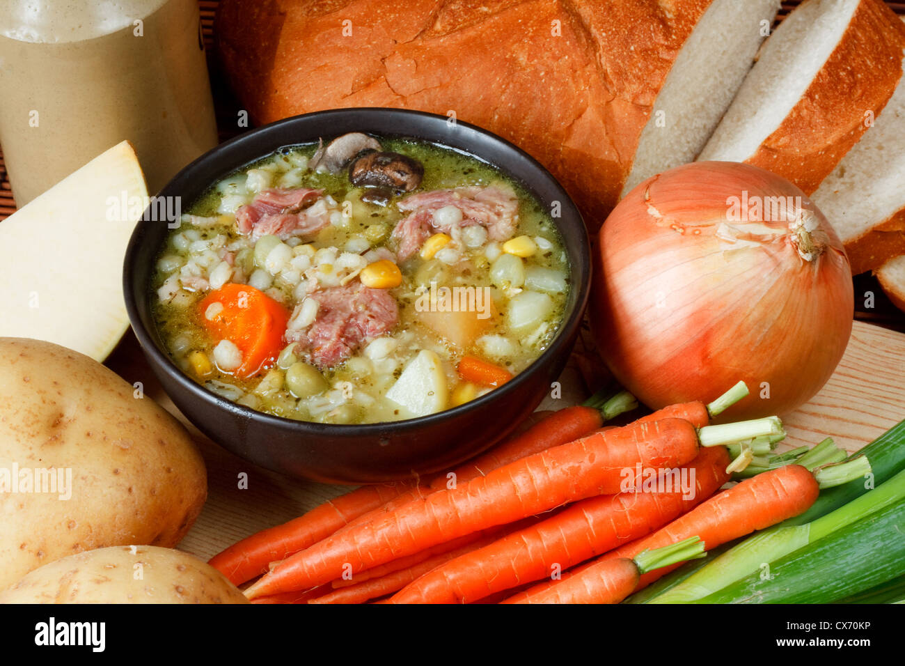 Bowl of ham broth in kitchen setting surrounded by ingredients, crusty bread and butter Stock Photo