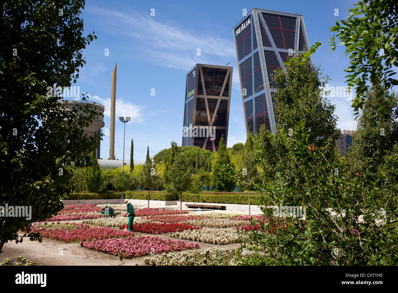 A gardener tends to flowers in the Parque Cuarto Deposito, Canal de Isabell II in front of the two leaning towers,Torres Kio, Stock Photo