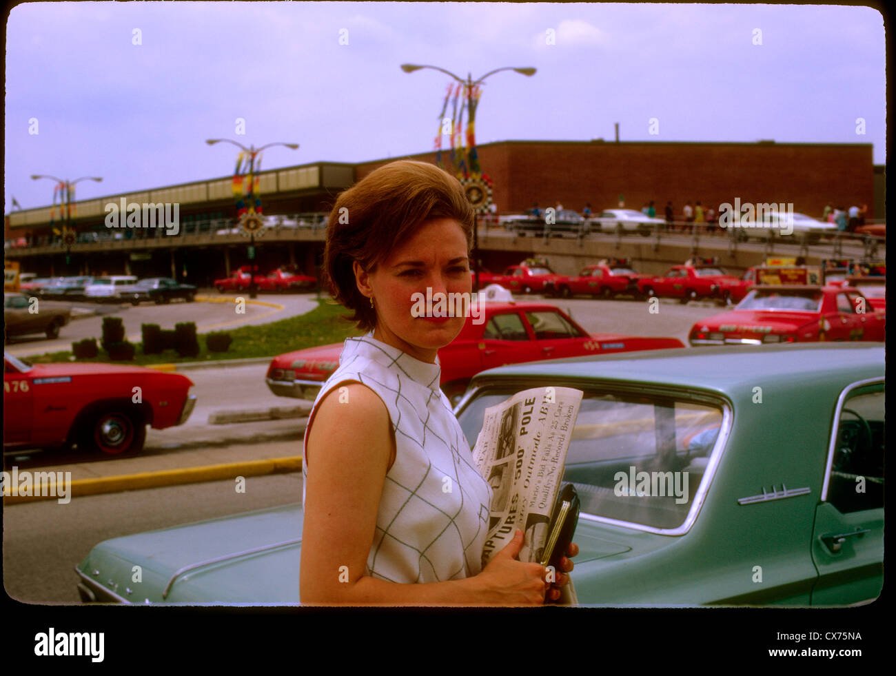 woman waiting at indianapolis airport holding indianapolis star newspaper may 1968 pole winner portrait taxis cars Stock Photo