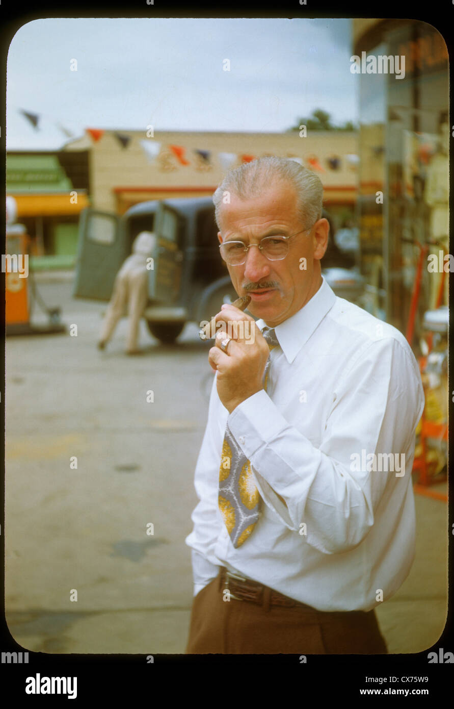 older man smoking cigarette outside hardware store gas pumps indiana 1940s kodachrome slide vertical portrait wealthy white male Stock Photo