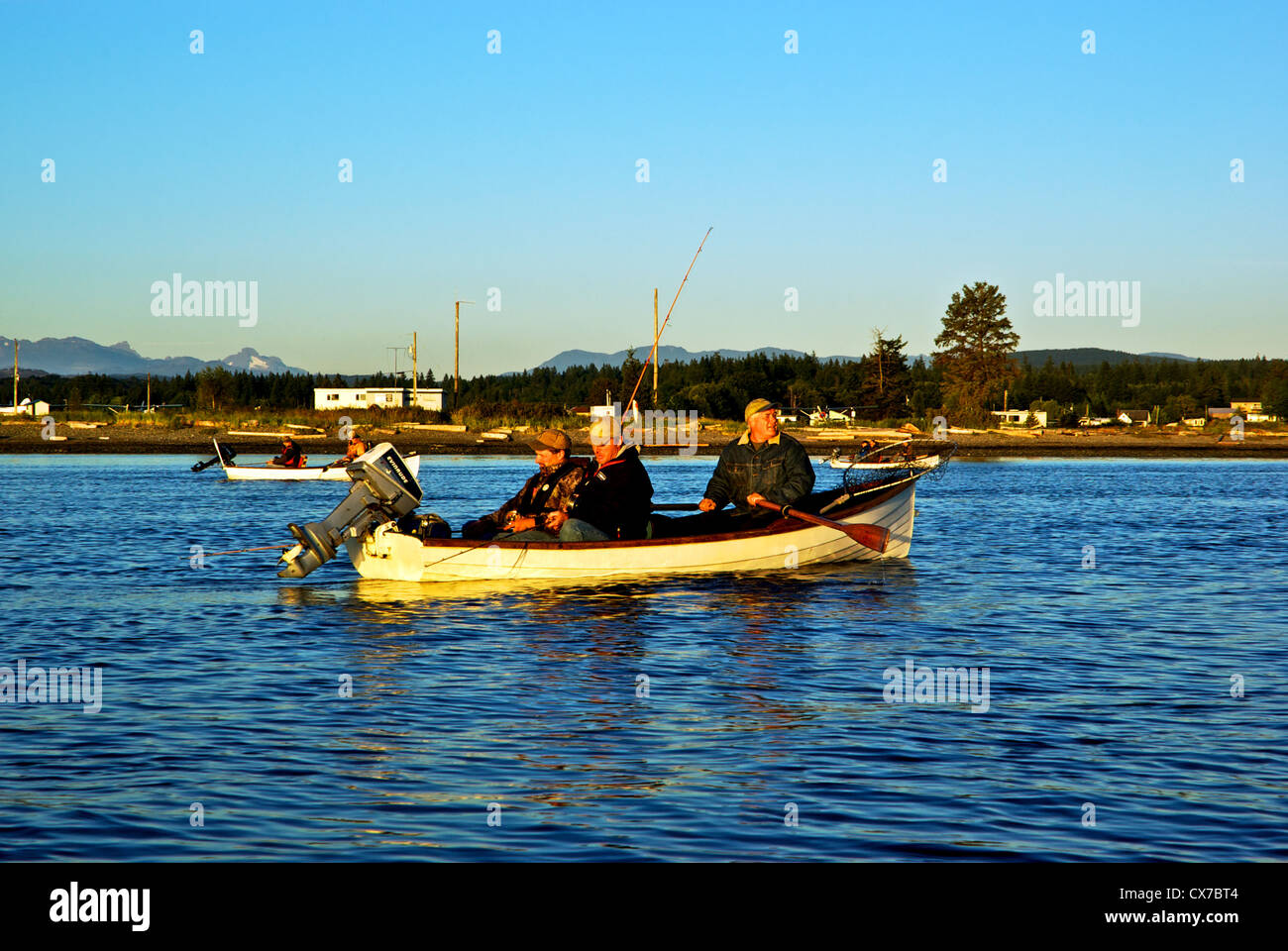 Guide and anglers rowing traditional rowboat to fish for chinook in Tyee Pool at mouth of Campbell River BC Canada at sunrise Stock Photo