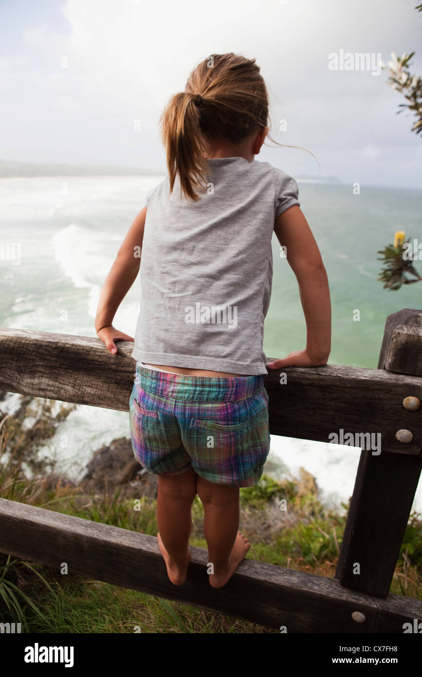 Girl Standing On The Rail Of A Wooden Fence Looking Out At The Ocean; Broken Heads, New South Wales, Australia Stock Photo
