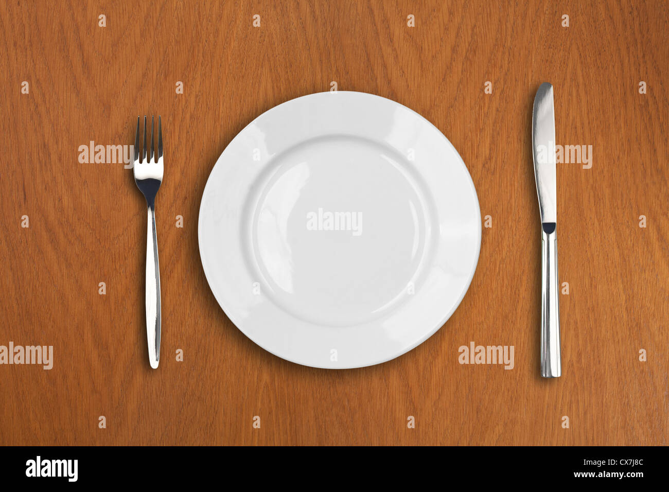 round white plate, knife and fork on wooden table Stock Photo