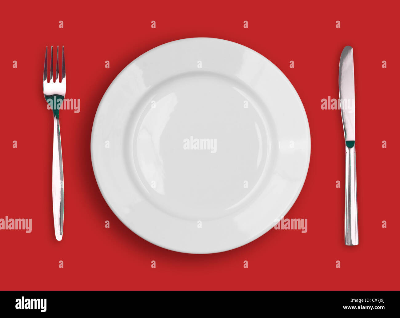 Knife, white plate and fork on red background Stock Photo