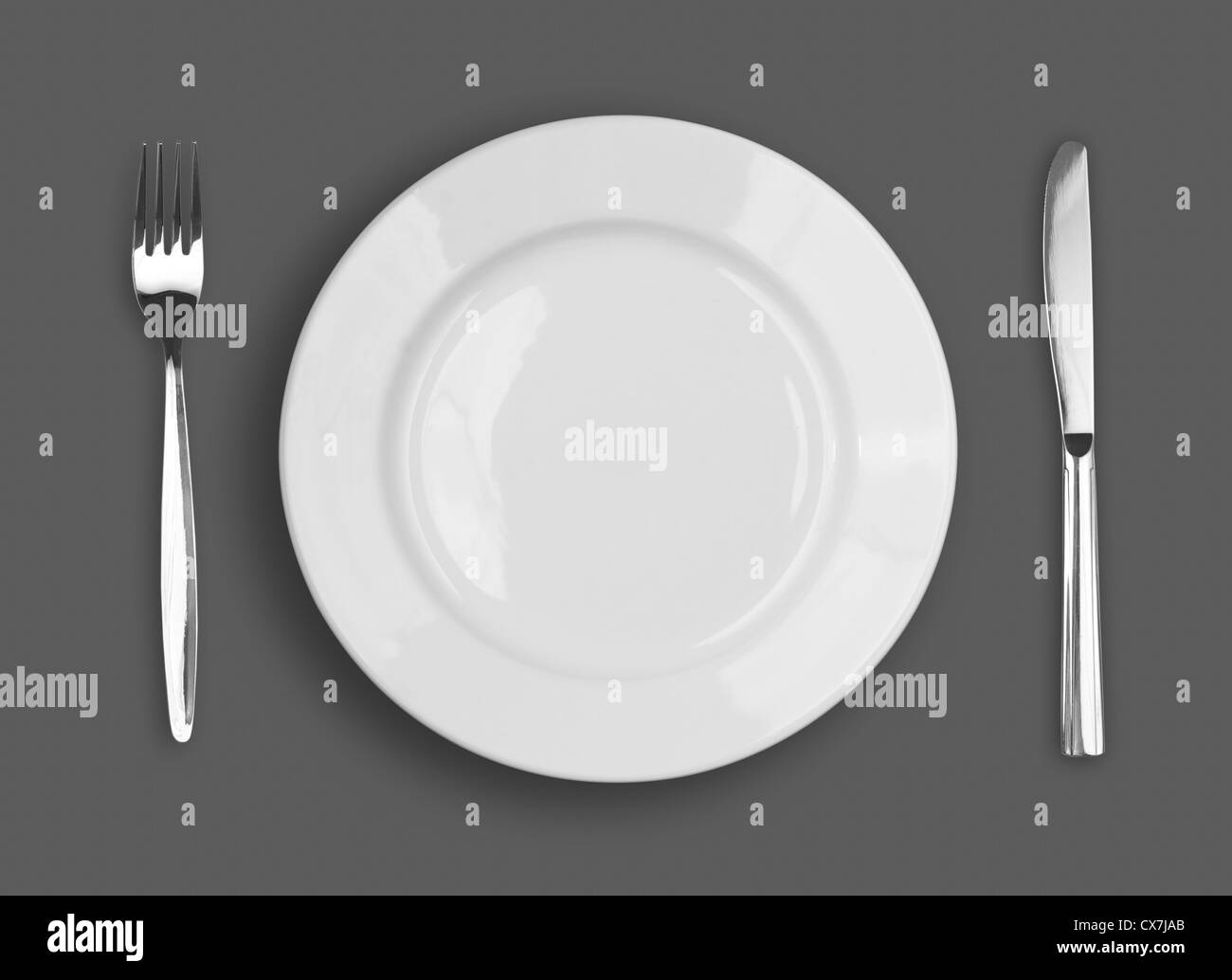 Knife, white plate and fork on gray background Stock Photo