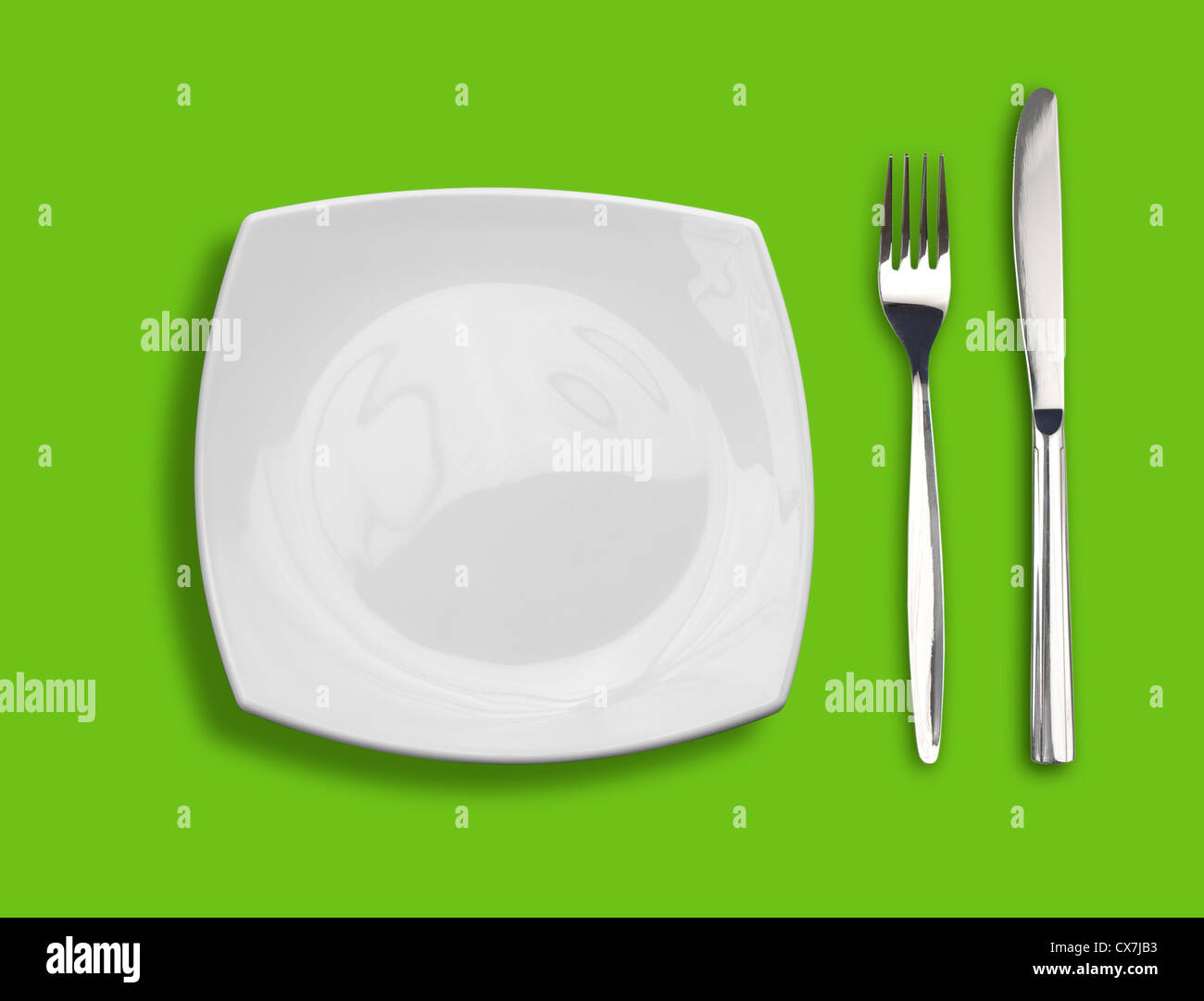 Knife, square white plate and fork on green background Stock Photo