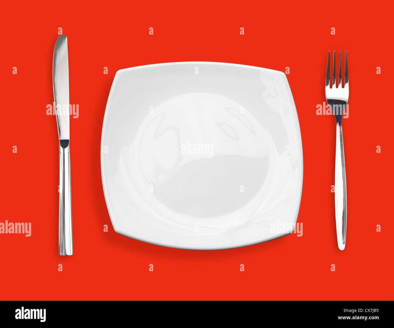 Knife, square white plate and fork on red background Stock Photo