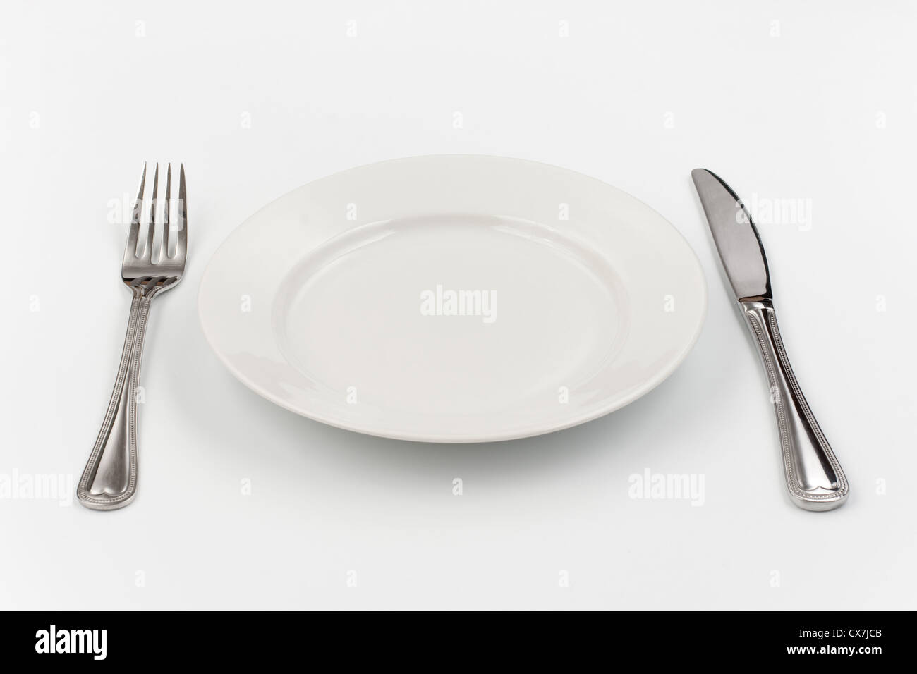 Place setting for one person. Knife, white plate and fork. Stock Photo