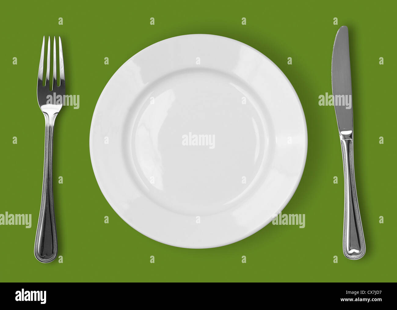 Knife, white plate and fork on green background Stock Photo