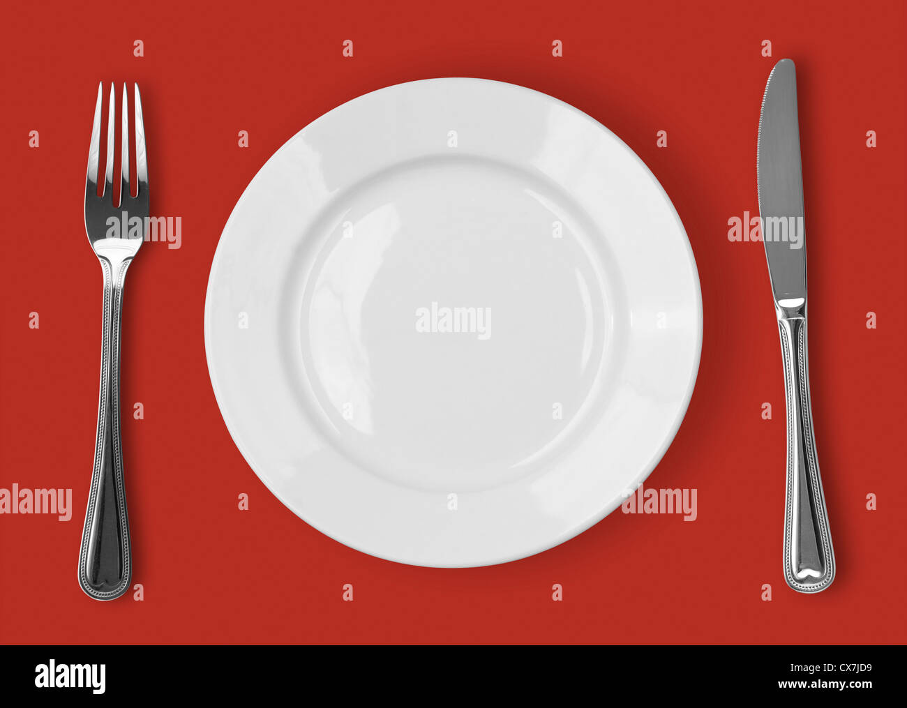 Knife, white plate and fork on red background Stock Photo