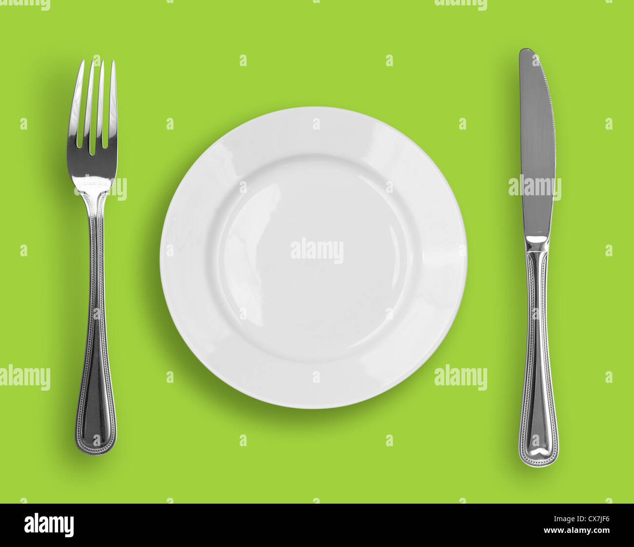 Knife, white plate and fork on green background Stock Photo