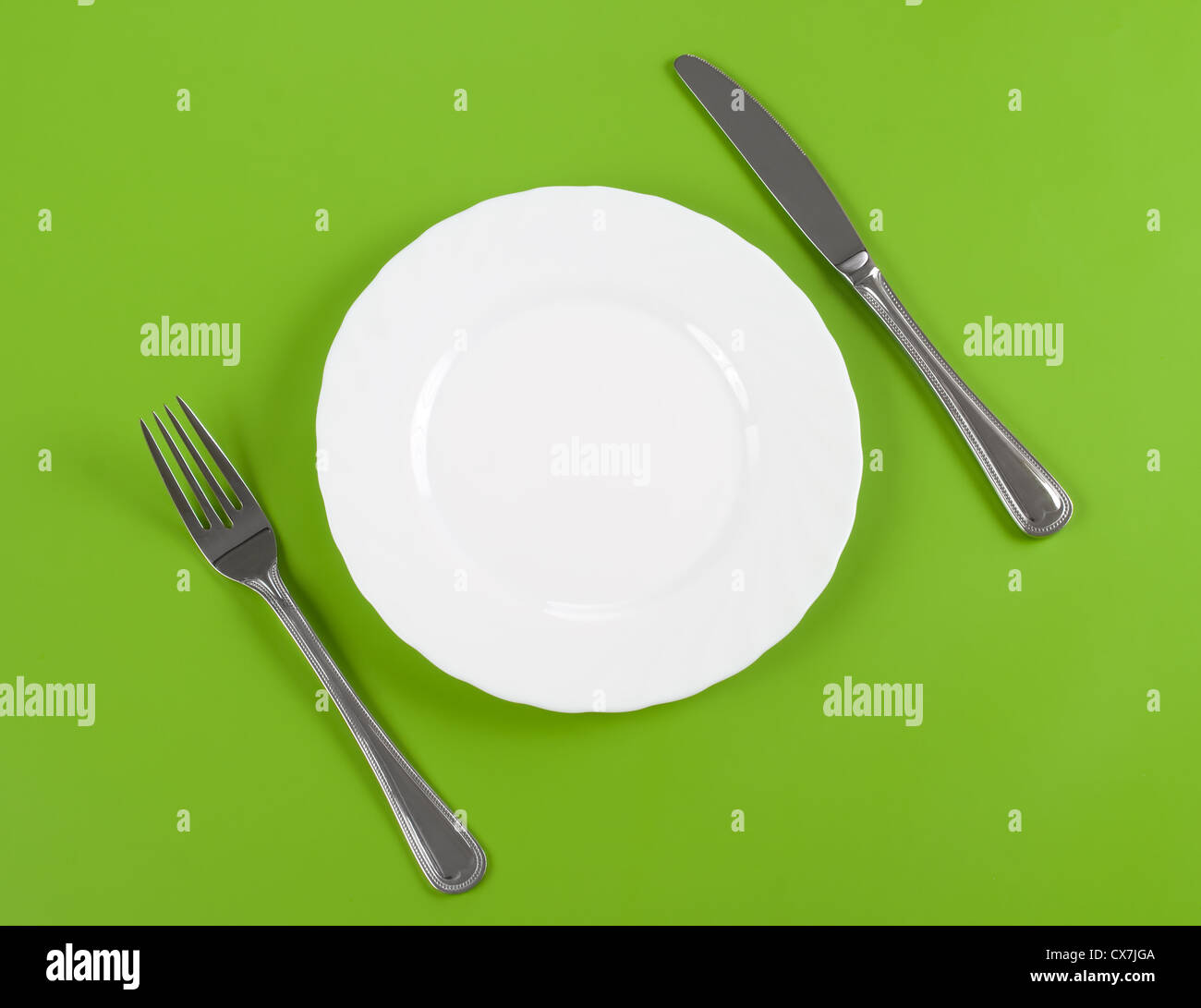 Knife, white round plate and fork on green background Stock Photo