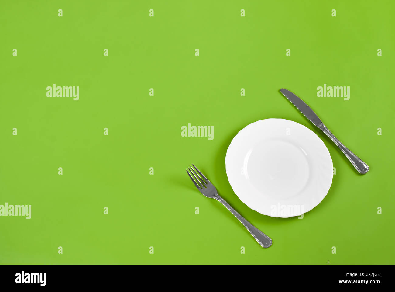 Knife, white round plate and fork on green background with free space Stock Photo