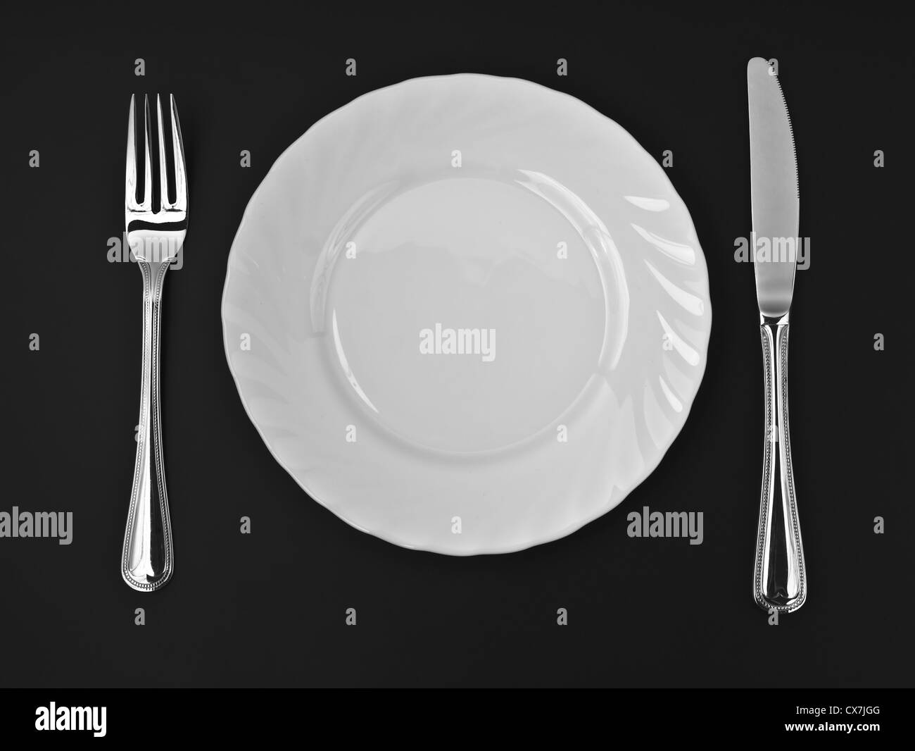 Knife, white plate and fork on black background Stock Photo