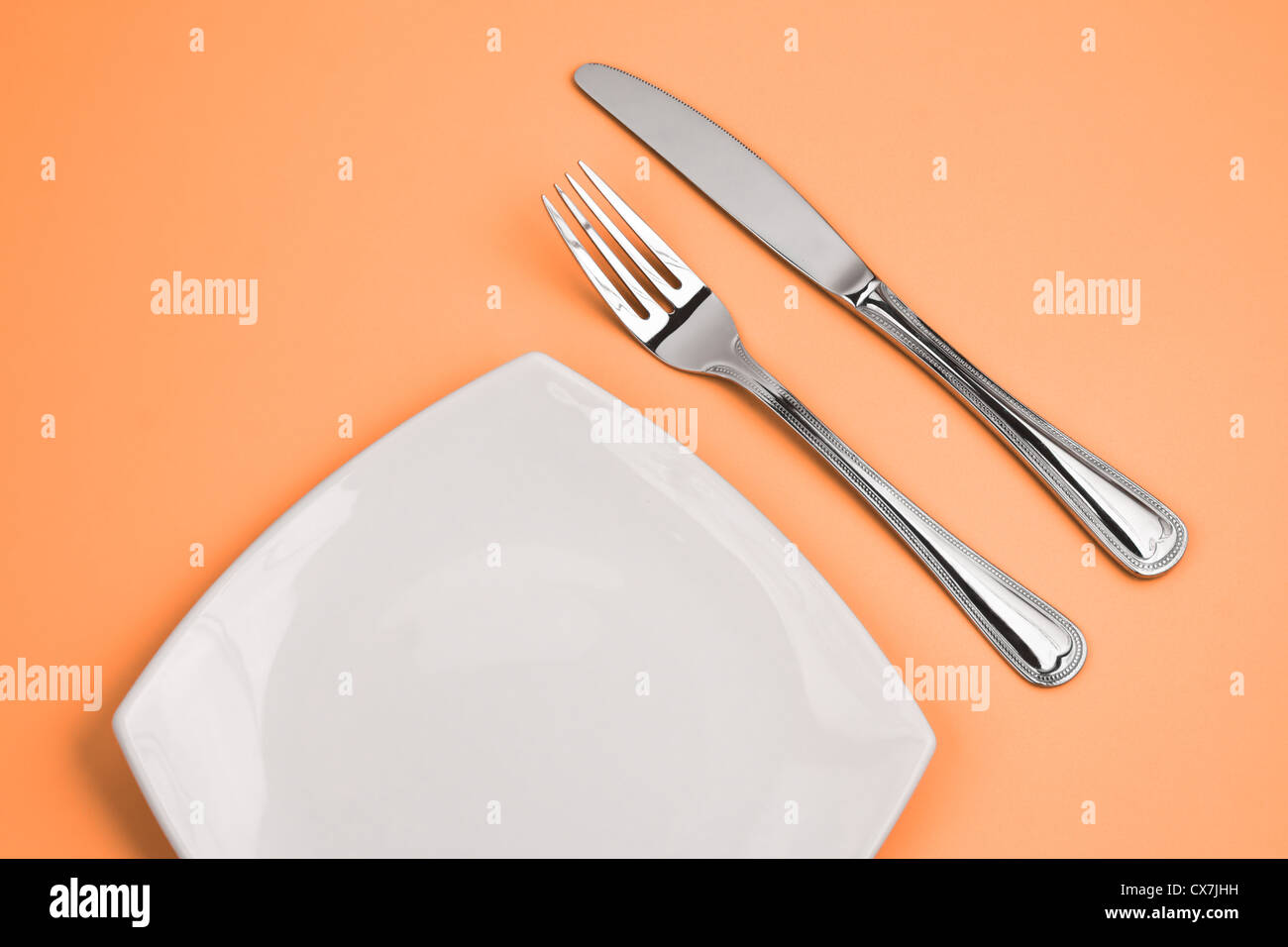 Knife, square white plate and fork on pink background Stock Photo - Alamy