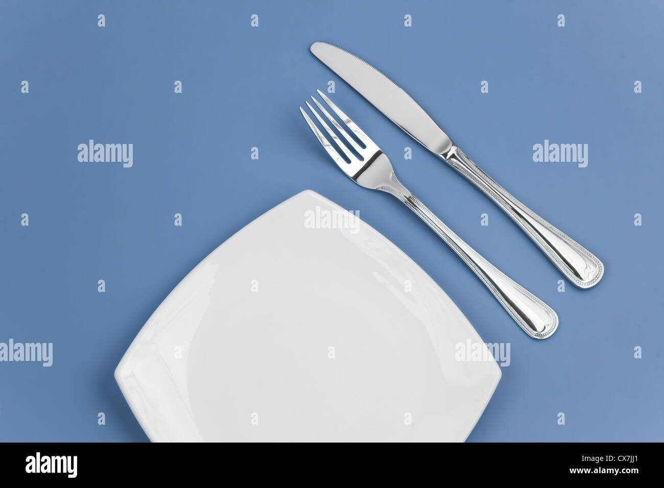 Knife, square white plate and fork on blue background Stock Photo