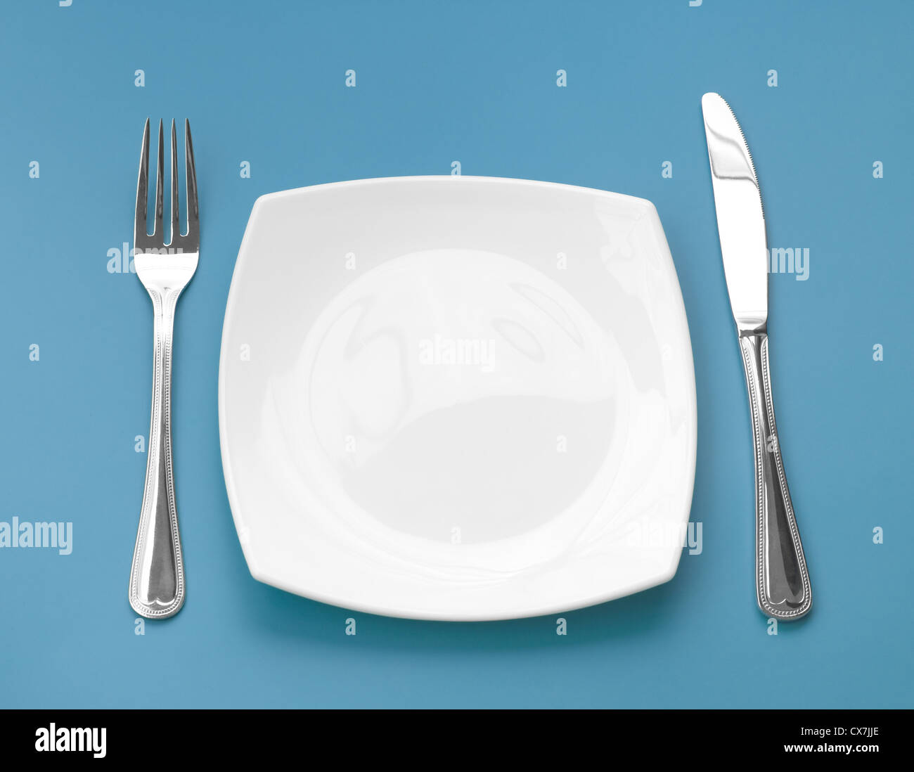 Knife, square white plate and fork on green background Stock Photo