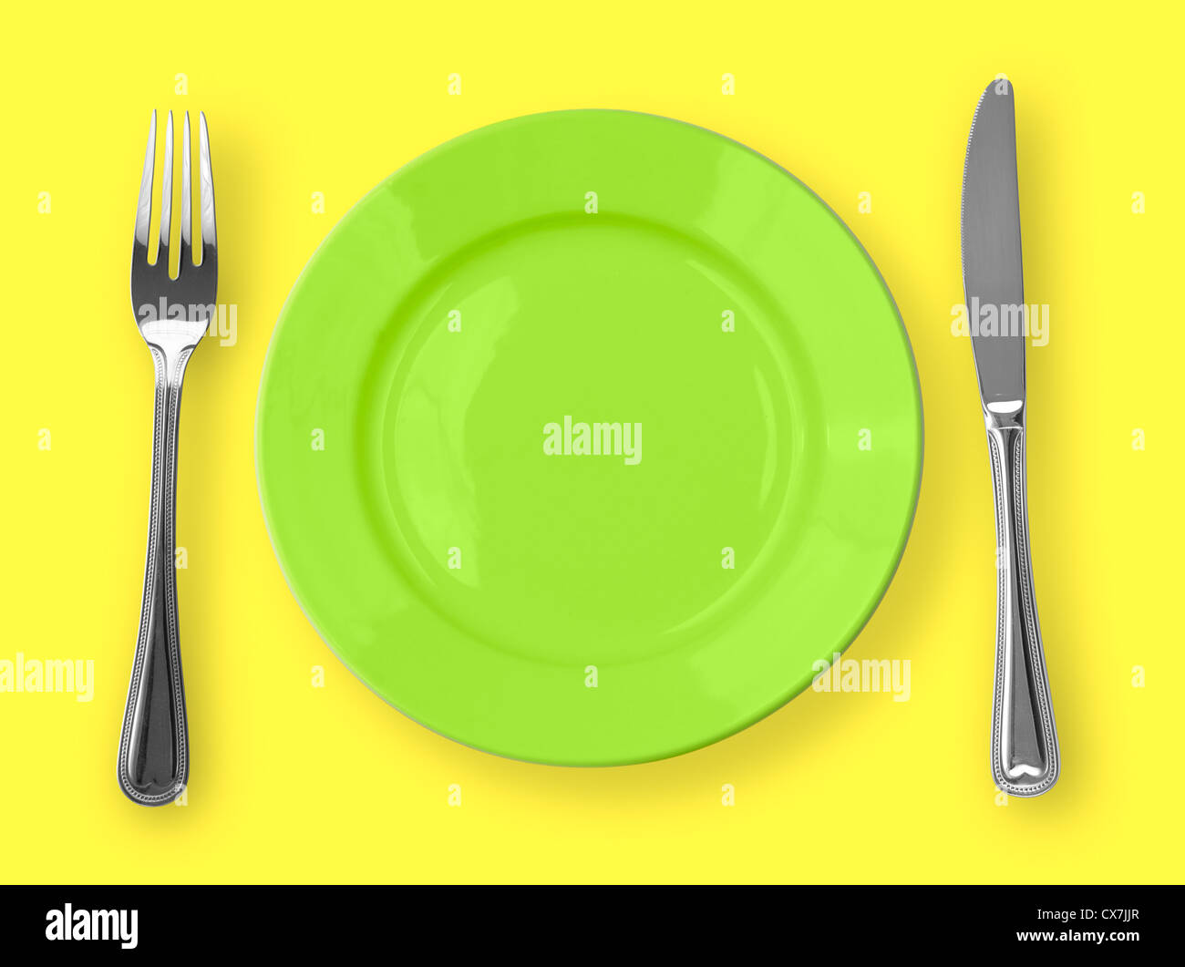 Knife, green plate and fork on yellow background Stock Photo