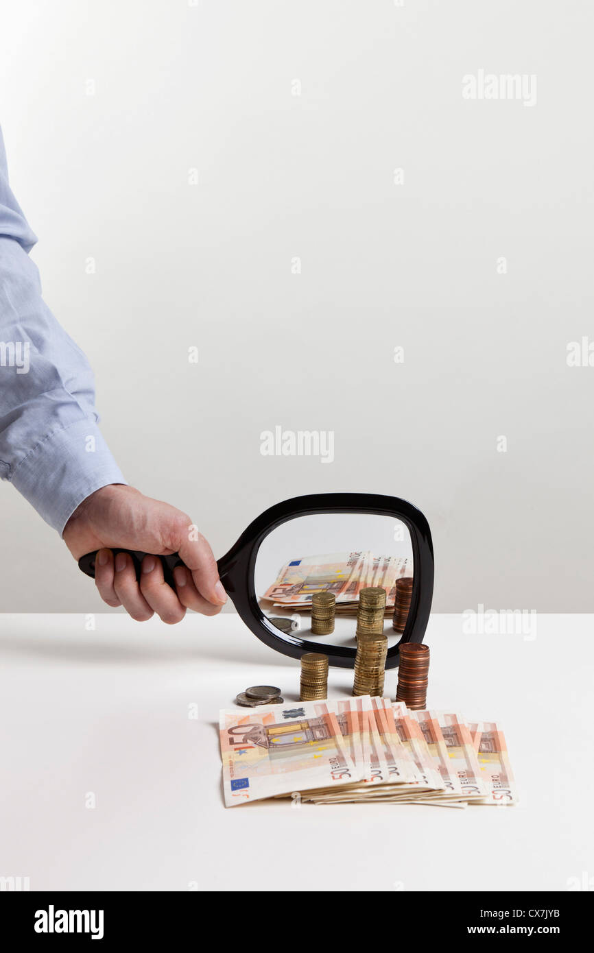 A man holding a hand mirror up to a pile of European Union currency Stock Photo
