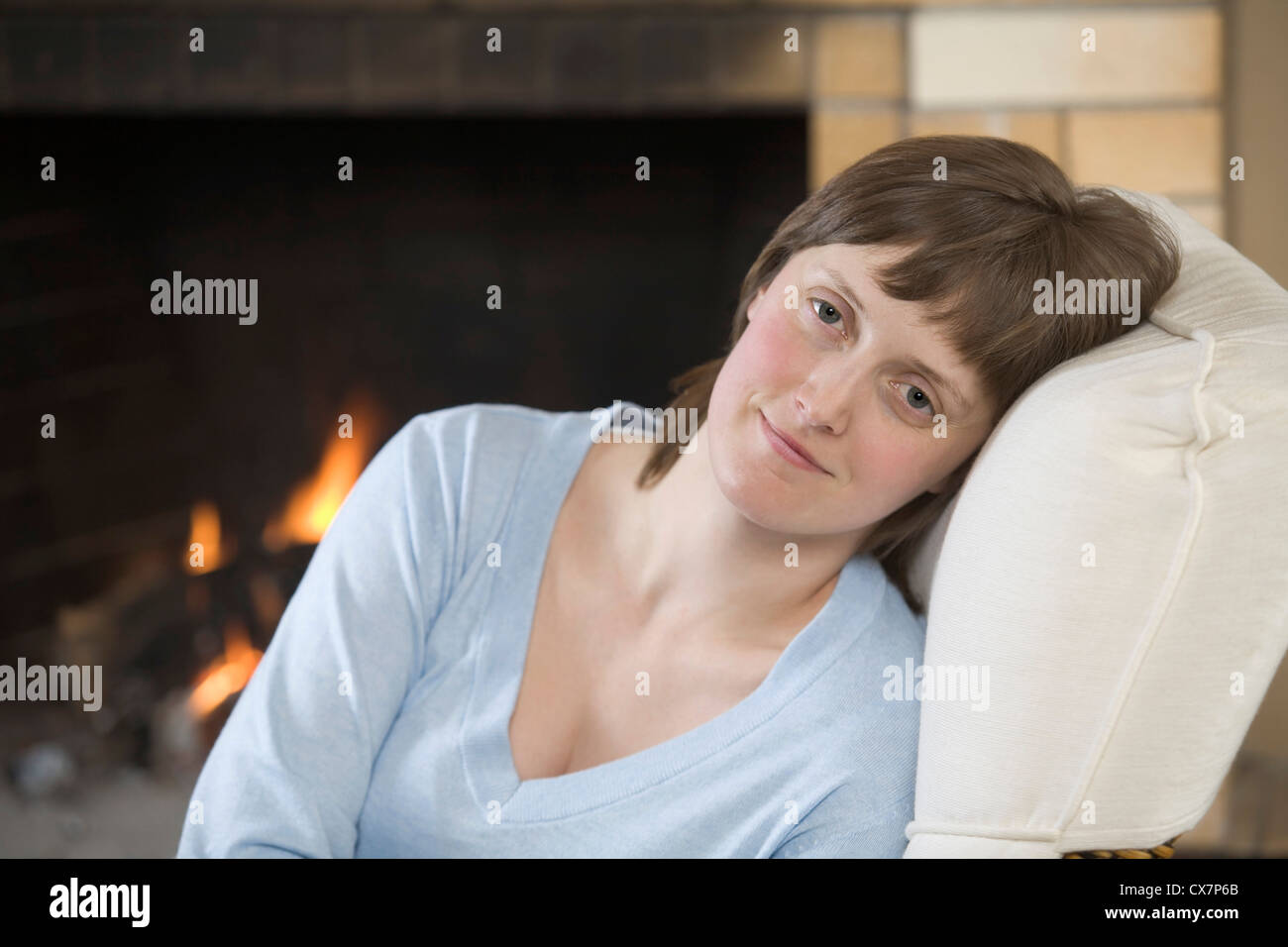 A serene young woman sitting near a roaring fire Stock Photo