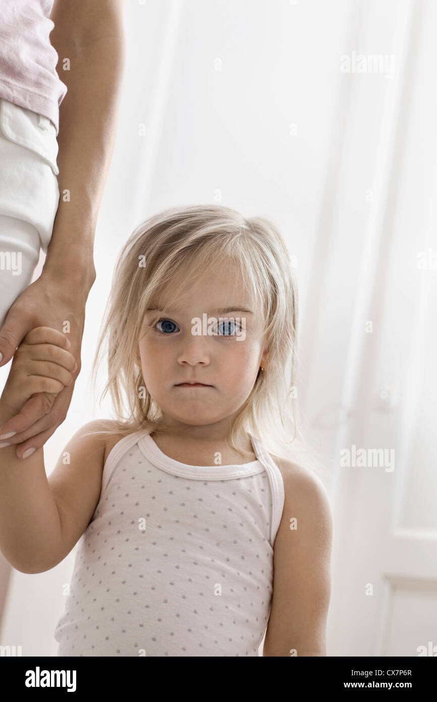 A young girl holding her mother's hand, staring into the camera Stock Photo