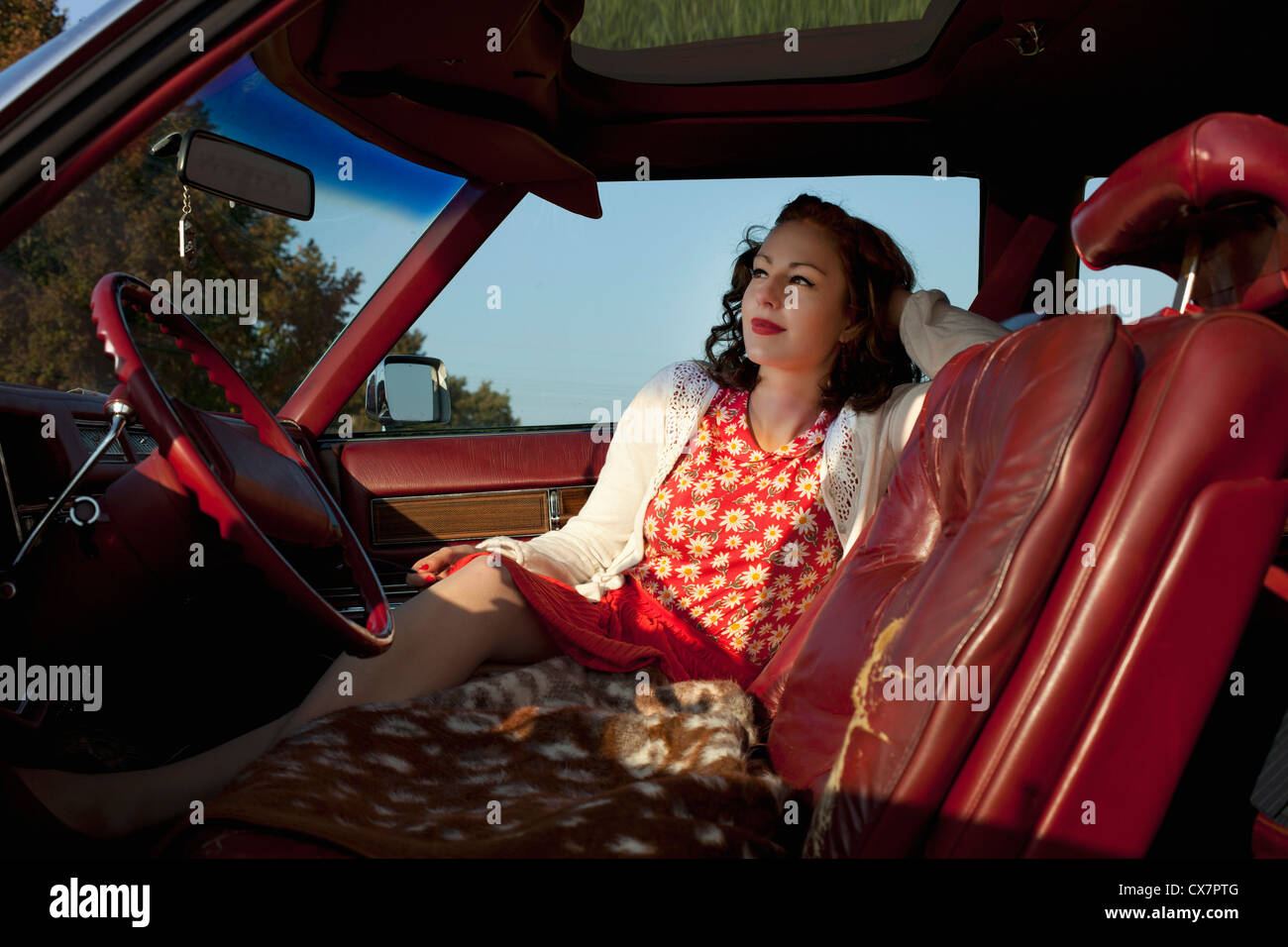 A pretty rockabilly woman sitting in the front seat of a vintage car Stock Photo