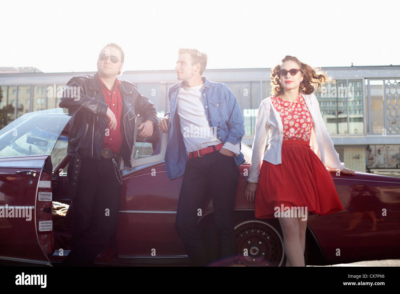 Three rockabilly friends leaning against a vintage car Stock Photo