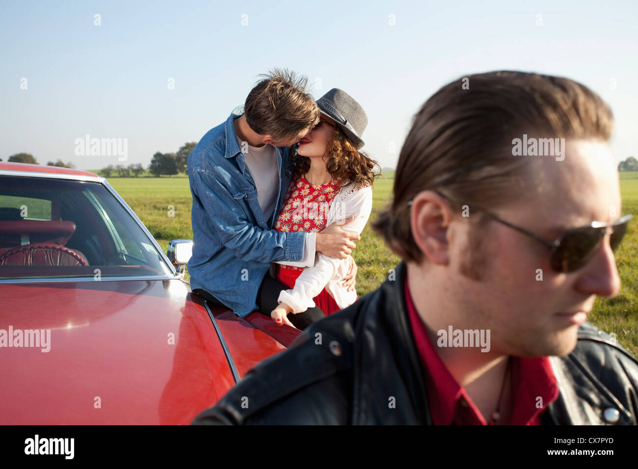 A rockabilly couple kissing while leaning on a vintage car, man in foreground Stock Photo