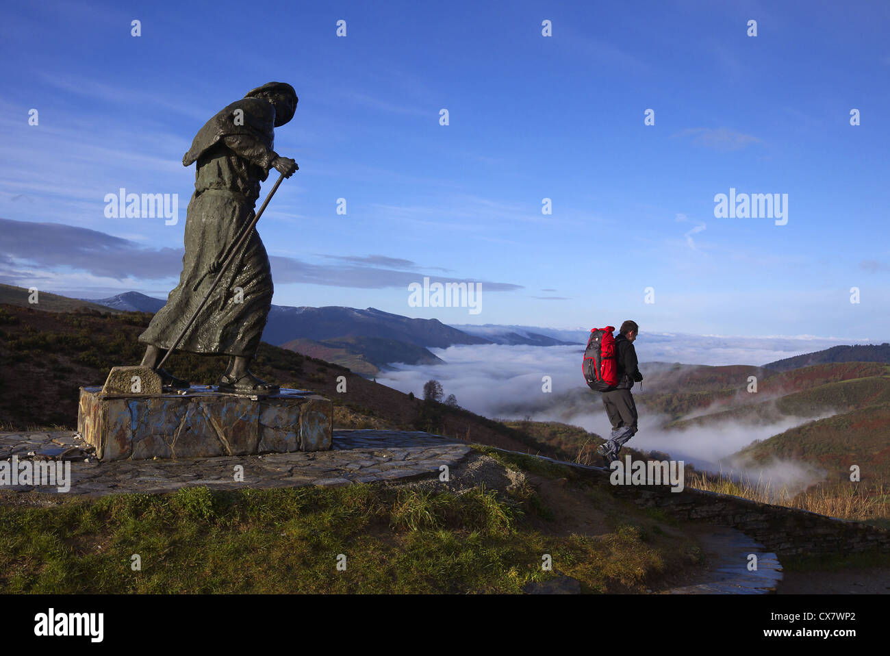 A modern pilgrim passes a statue of a medieval pilgrim, San Roque, near Linares, Spain. Stock Photo