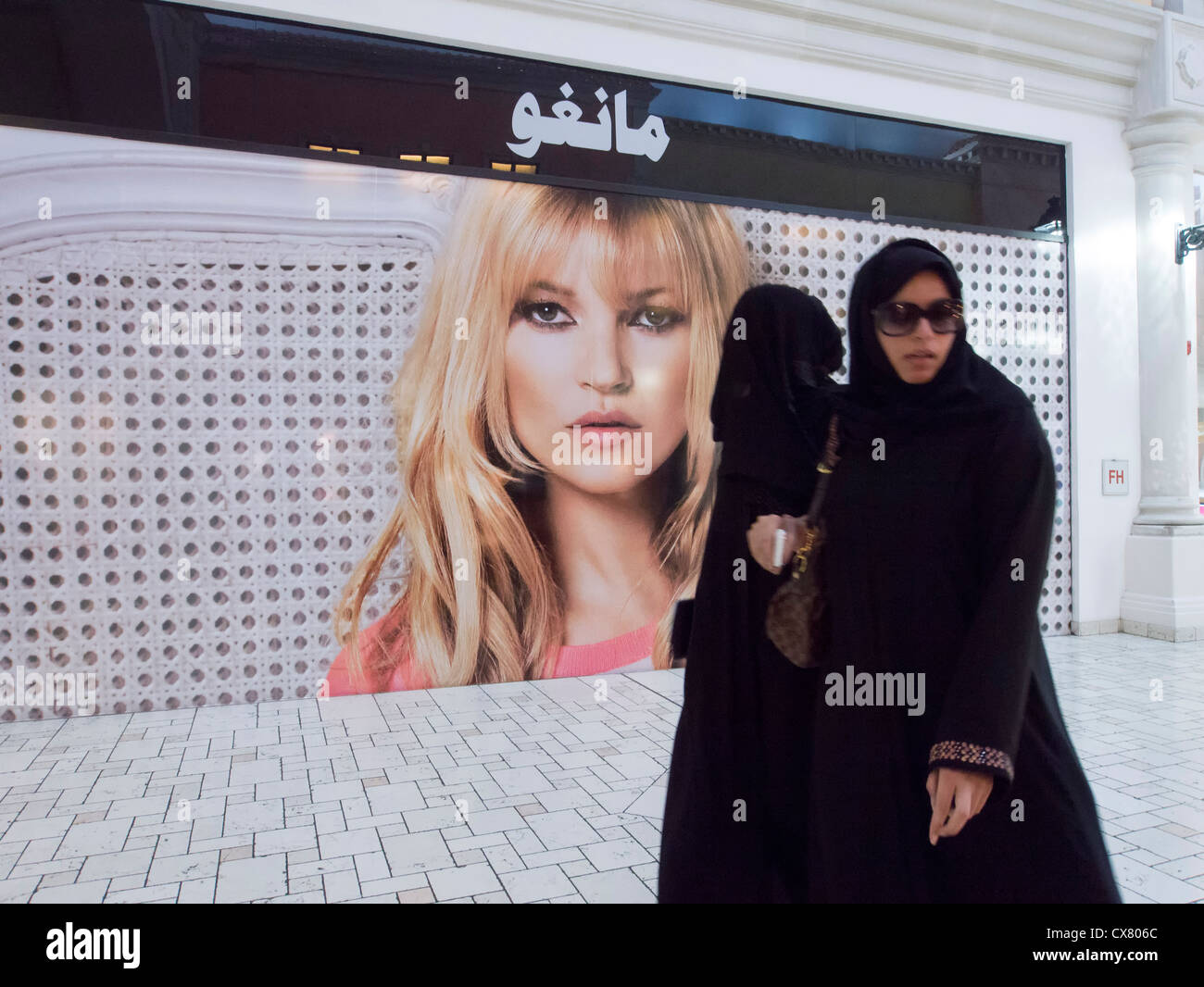 Arab women walk past western billboard on shop in upmarket Villaggio shopping mall in Doha Qatar Stock Photo