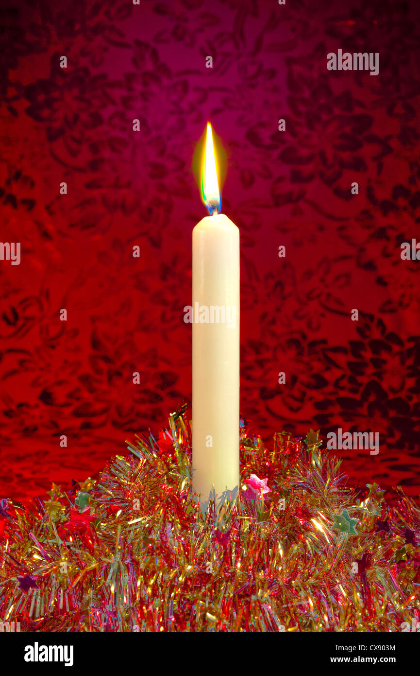 A festive Christmas candle and glittering tinsel on a red background, treated in a surrealistic manner Stock Photo