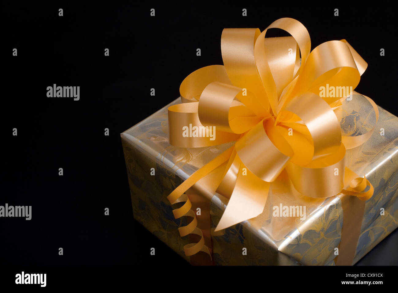 Nice gift packed in golden paper with yellow bow on black background Stock Photo