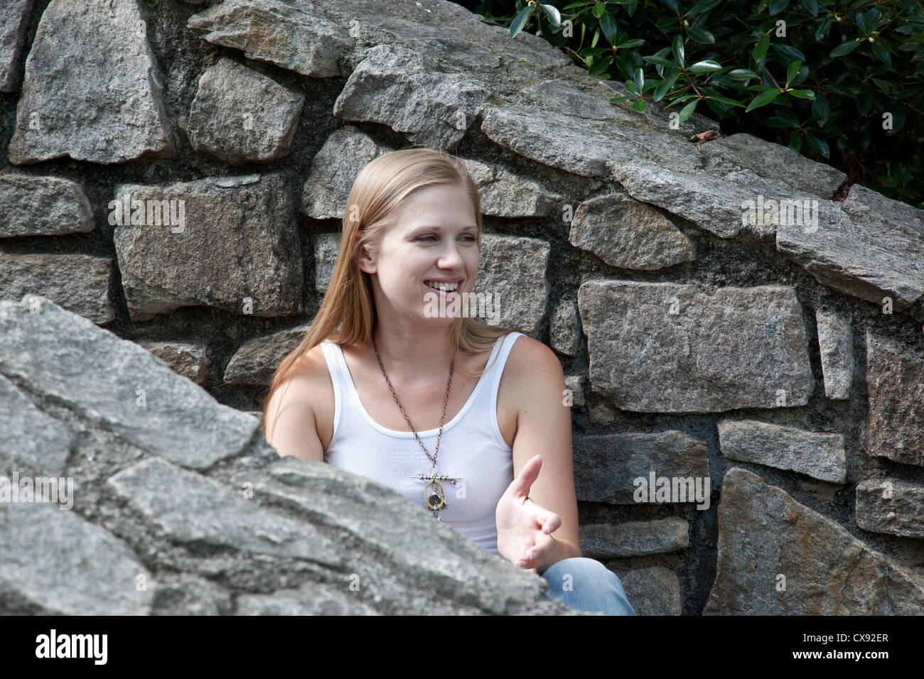 Pretty blond woman sitting outside on stone steps and looking to the right with a happy smile Stock Photo