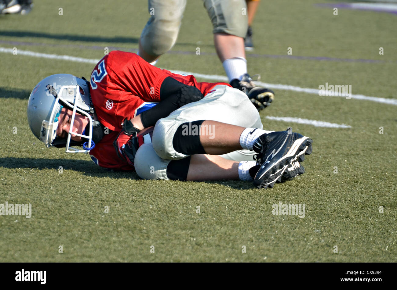 A young football player on the ground holding the ball after a missed