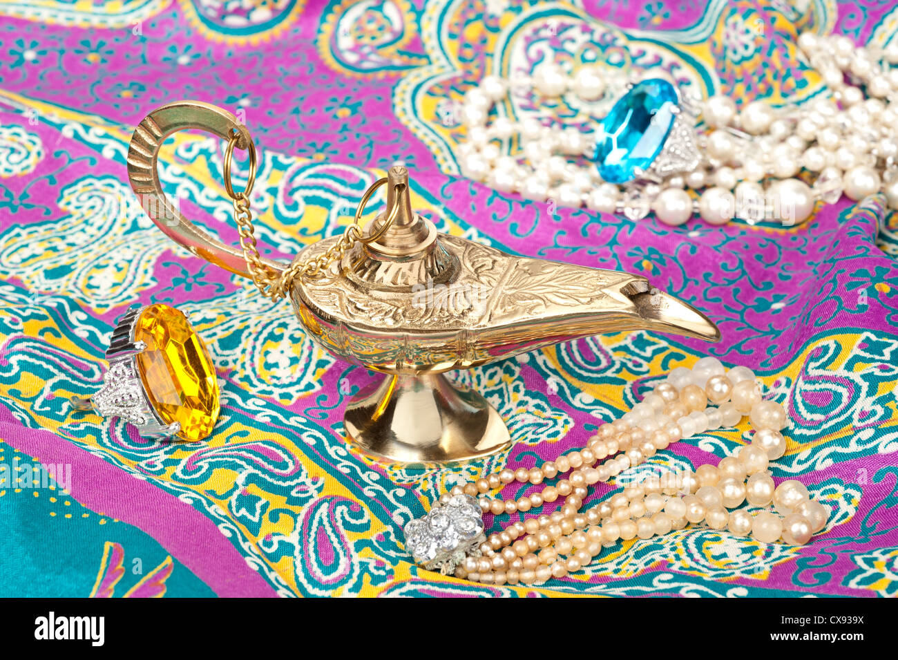 A magic oil lamp on top of gypsy clothing and surrounded by jewelry. Stock Photo