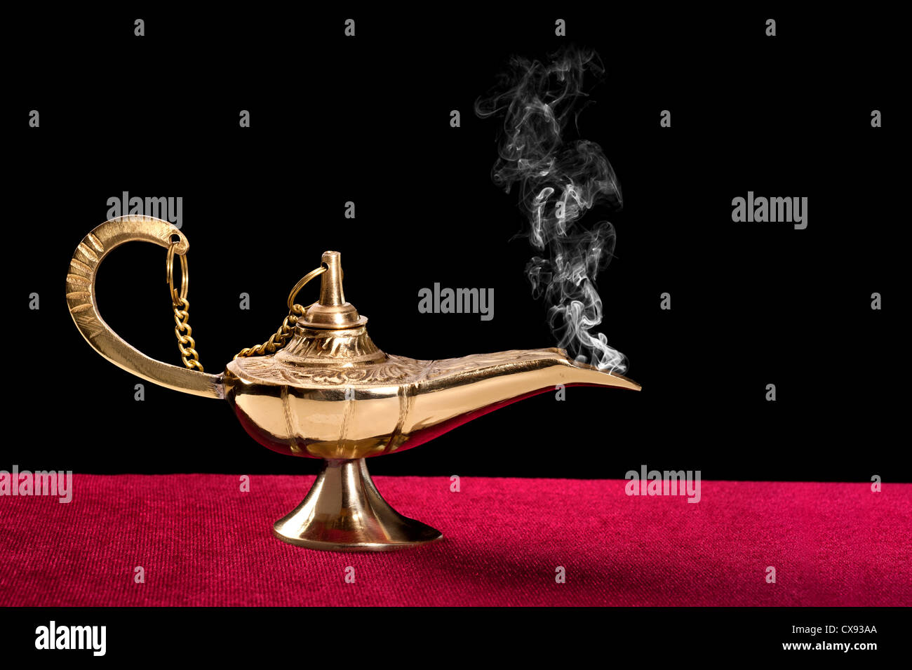 An ancient magic lamp on a red felt table top disperses a stream of mysterious smoke. Stock Photo