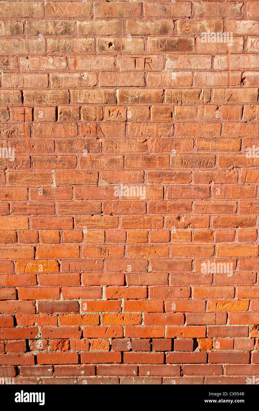 An old, red brick wall that has had many names carved into it. Stock Photo