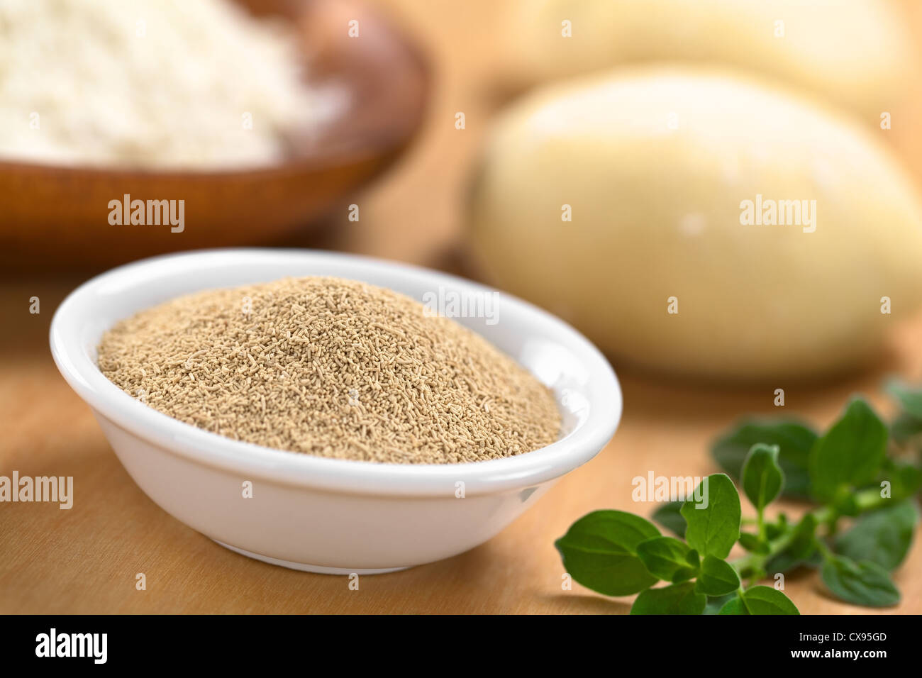 Active dry yeast in small bowl with fresh oregano on the side, flour and dough in the back Stock Photo