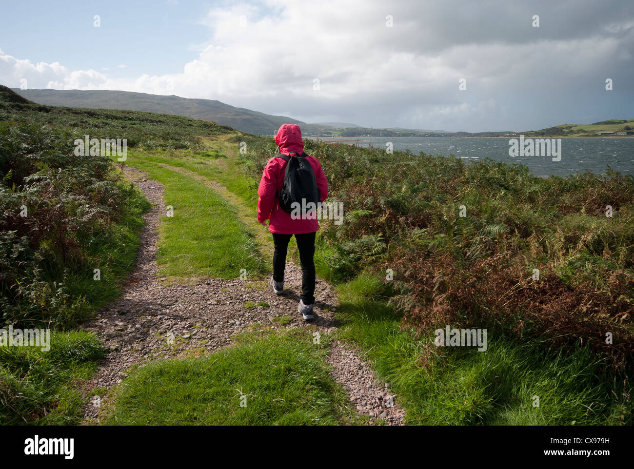 Rear View Of A Woman Person Walking Through The Countryside Wearing Waterproof Clothing and A Rucksack Stock Photo